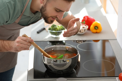 Young man cooking delicious soup in kitchen