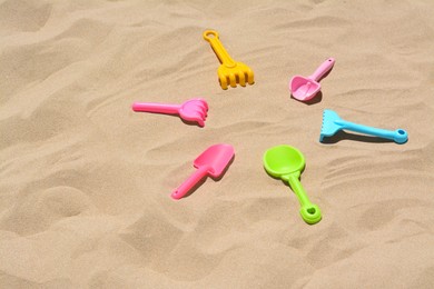 Bright plastic rakes and shovels on sand, space for text. Beach toys
