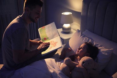 Father reading bedtime story to his daughter at home
