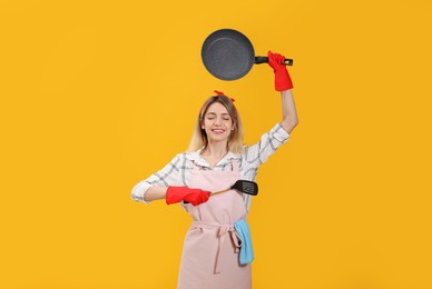 Photo of Young housewife meditating with frying pan and spatula on yellow background