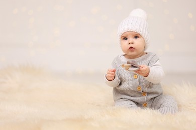 Photo of Cute baby with toy on fluffy carpet against blurred festive lights, space for text. Winter holiday