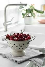 Fresh ripe cherries with water drops in colander on countertop indoors