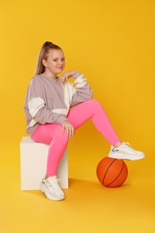 Cute indie girl with basketball ball on yellow background
