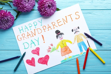 Beautiful drawing with phrase Happy Grandparents Day on blue wooden table, flat lay
