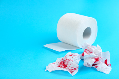 Sheets of toilet paper with blood on light blue background, space for text. Hemorrhoid problems