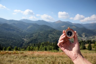 Woman with compass in mountains, closeup. Space for text