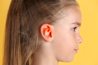 Little girl on yellow background, closeup. Hearing problem