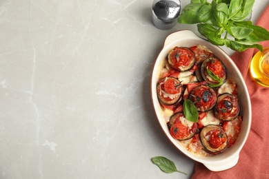 Baked eggplant with tomatoes, cheese and basil in dishware on light marble table, flat lay. Space for text