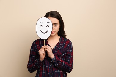 Sad woman hiding behind happy paper face on beige background