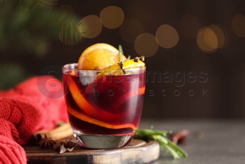 Glass with aromatic mulled wine on grey table against festive lights. Space for text