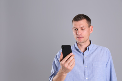Man unlocking smartphone with facial scanner on grey background, space for text. Biometric verification