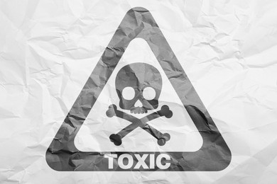 Hazard warning sign (skull-and-crossbones symbol and word TOXIC) on crumpled white paper, top view