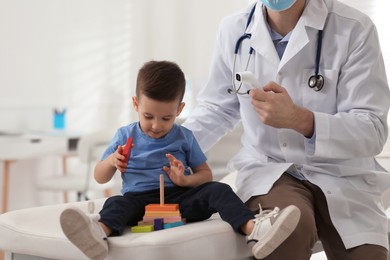 Pediatrician checking little boy's temperature at hospital