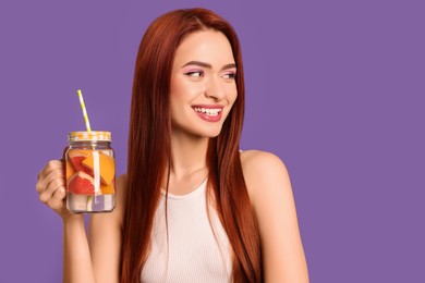 Photo of Happy woman with red dyed hair and refreshing grapefruit drink on purple background