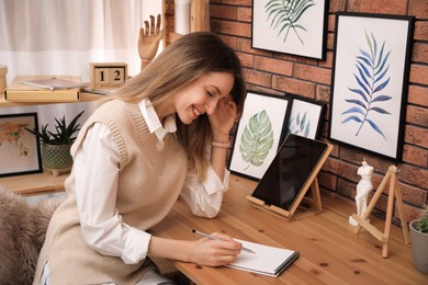 Young woman drawing in sketchbook with pencil at wooden table indoors