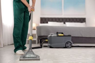 Professional janitor removing dirt from carpet with vacuum cleaner in bedroom, closeup. Space for text