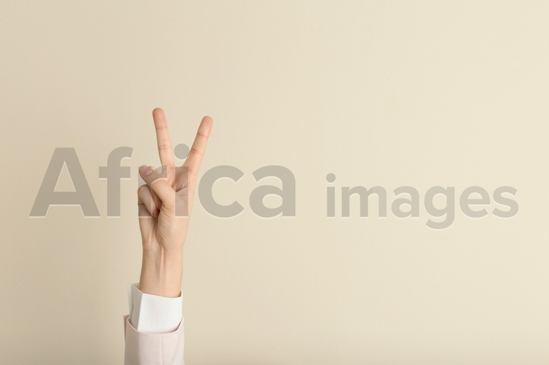 Photo of Young woman showing victory gesture on color background. Space for text