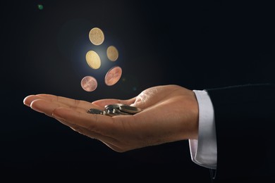 Man and coins falling into his hand on black background, closeup