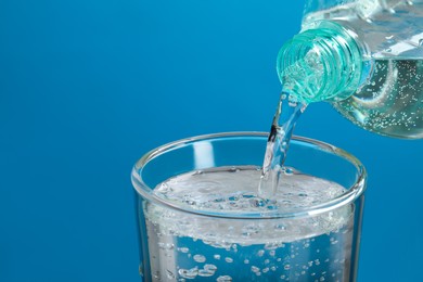 Photo of Pouring soda water from bottle into glass on light blue background, closeup. Space for text
