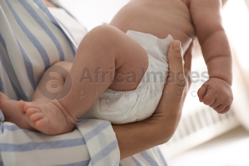Photo of Mother holding her cute child in diaper at home, closeup