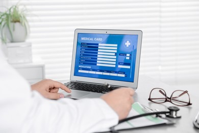 Doctor using laptop to fill out patient's medical card at table in clinic, closeup
