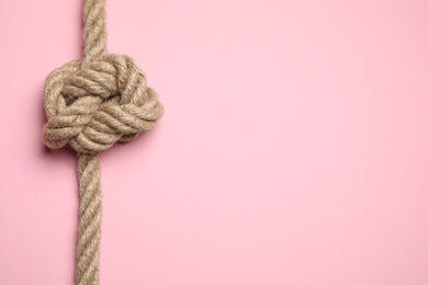 Top view of linen rope with knot on pink background, space for text. Unity concept