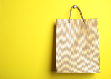 Gold shopping paper bag on yellow background, space for text