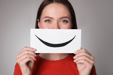 Woman holding sheet of paper with smile on grey background