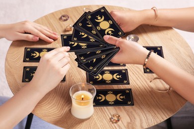 Photo of Woman pulling one tarot card at table indoors, closeup. Fortune telling