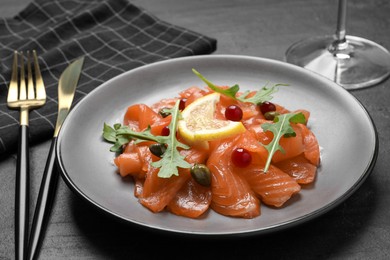 Salmon carpaccio with capers, cranberries, arugula and lemon served on black table