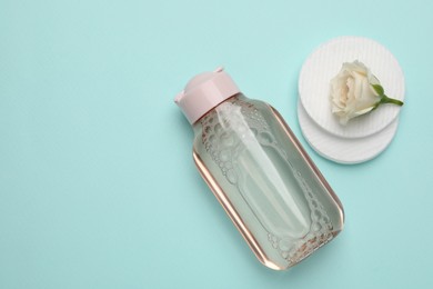 Bottle of micellar cleansing water, cotton pads and flower on turquoise background, flat lay. Space for text
