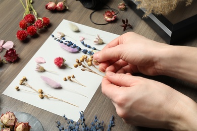Woman making herbarium of dry flowers at wooden table, closeup