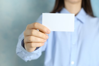 Photo of Woman holding blank business card on light blue background, closeup. Mockup for design
