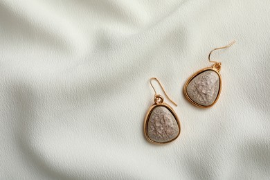 Elegant earrings on white fabric, flat lay with space for text. Stylish bijouterie