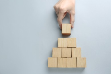 Woman arranging blank wooden cubes on light background, top view. Space for text