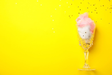 Glass with cotton candy on yellow background, top view. Space for text