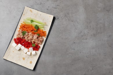 Photo of Delicious tortilla with tuna and vegetables on grey table, top view. Cooking shawarma