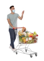 Man with protective mask and shopping cart full of groceries on white background