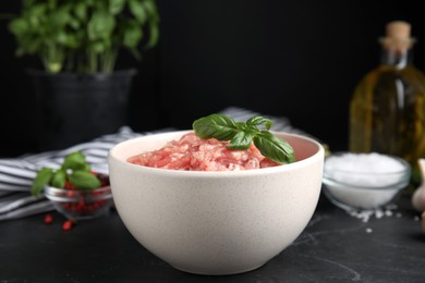 Raw chicken minced meat with basil on black table, closeup