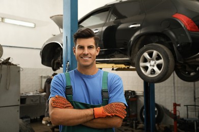 Photo of Portrait of professional mechanic near lifted car at automobile repair shop