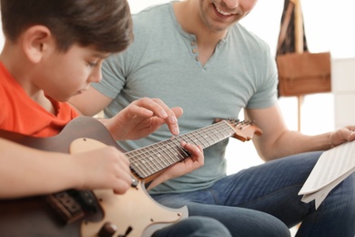 Little boy playing guitar with his teacher at music lesson, closeup. Learning notes