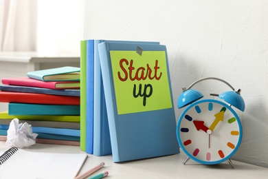 Photo of Book with words Start Up, stationery and alarm clock on white wooden table indoors
