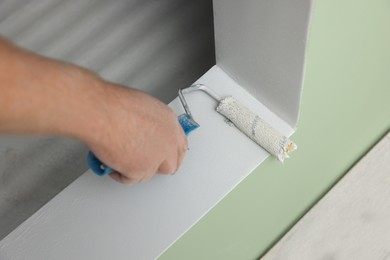 Photo of Worker using roller to paint wall with white dye indoors, closeup