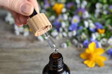 Woman pouring essential oil from pipette into bottle on table, closeup