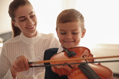 Young woman teaching little boy to play violin indoors