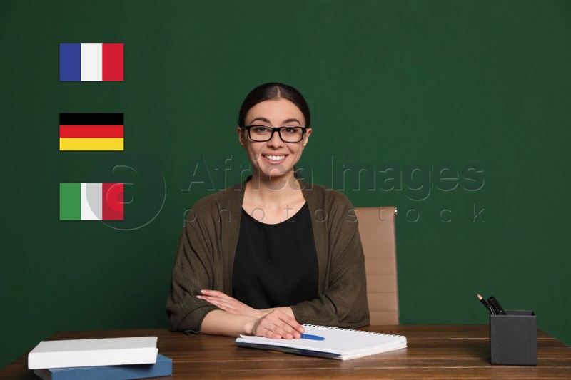 Portrait of foreign languages teacher at wooden table and different flags green chalkboard