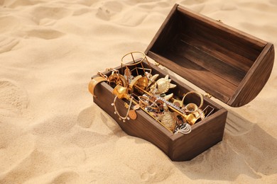 Photo of Open wooden chest with treasures on sand, space for text