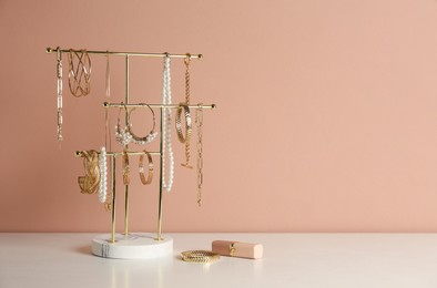 Holder with set of luxurious jewelry and lipstick on white table near pale pink wall, space for text
