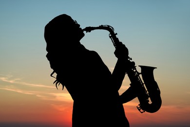 Silhouette of woman playing saxophone against beautiful sky at sunset