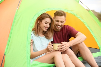 Young woman with mug and man in camping tent